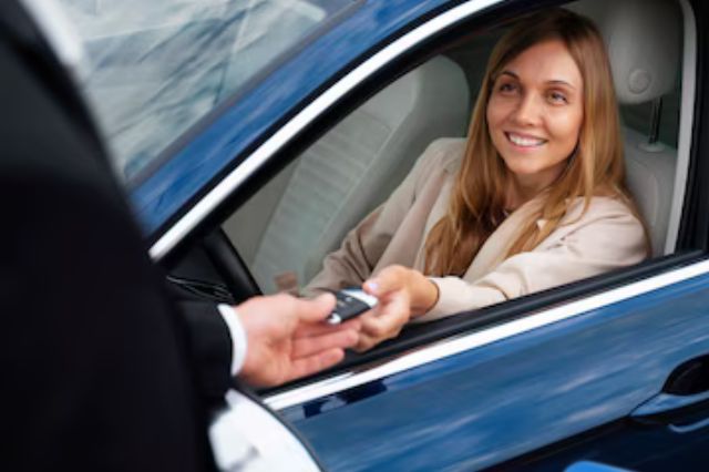 Mulher sorridente dentro de um carro azul recebendo as chaves de um homem em traje formal.